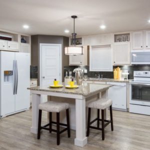 Modern manufactured home kitchen interior with a central island, bar stools, and stainless steel appliances.