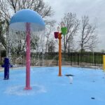 A colorful splash pad with various water features in a Michigan trailer park on a cloudy day.