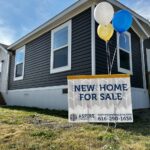 A new mobile home for sale with a sign and balloons in front of it.