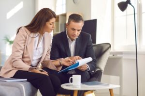 Two professionally dressed people sit together in an Aspire Communities office, reviewing documents in a bright space filled with natural light and a coffee cup on the table.