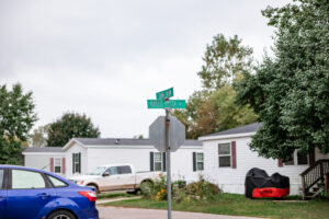 A street sign for Belle Vista Dr and Avalon Dr stands at an intersection in the Riverwood suburban neighborhood, surrounded by houses, cars, and trees.