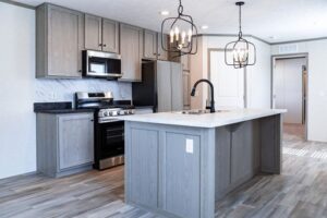 Modern kitchen in Hidden Glades with gray cabinets, stainless steel appliances, center island with sink and black faucet, pendant lights, and wood-style flooring.