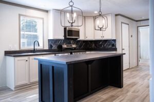 Modern kitchen in Hidden Glades with white cabinets, black island, marble backsplash, stainless steel appliances, pendant lighting, and light wood flooring.