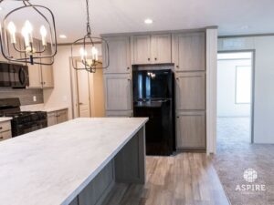 Modern kitchen in Hidden Glades with light wood cabinets, a black refrigerator, marble-look island, gas stove, and pendant lights. An adjacent carpeted room is visible in the background.