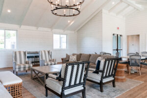 A spacious, bright living room with vaulted ceilings in Lakeview Village features neutral-toned sofas and chairs, a large chandelier, and a wooden coffee table on a light rug.
