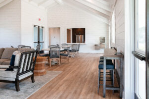 A modern, bright lounge area at Lakeview Village with high ceilings, assorted seating, wooden floors, and a water dispenser near large windows.