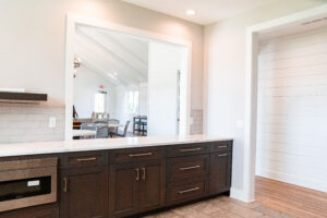 Modern Lakeview Village kitchen with dark cabinets, white countertops, and a large pass-through window overlooking a bright dining area with vaulted ceilings and wood flooring.