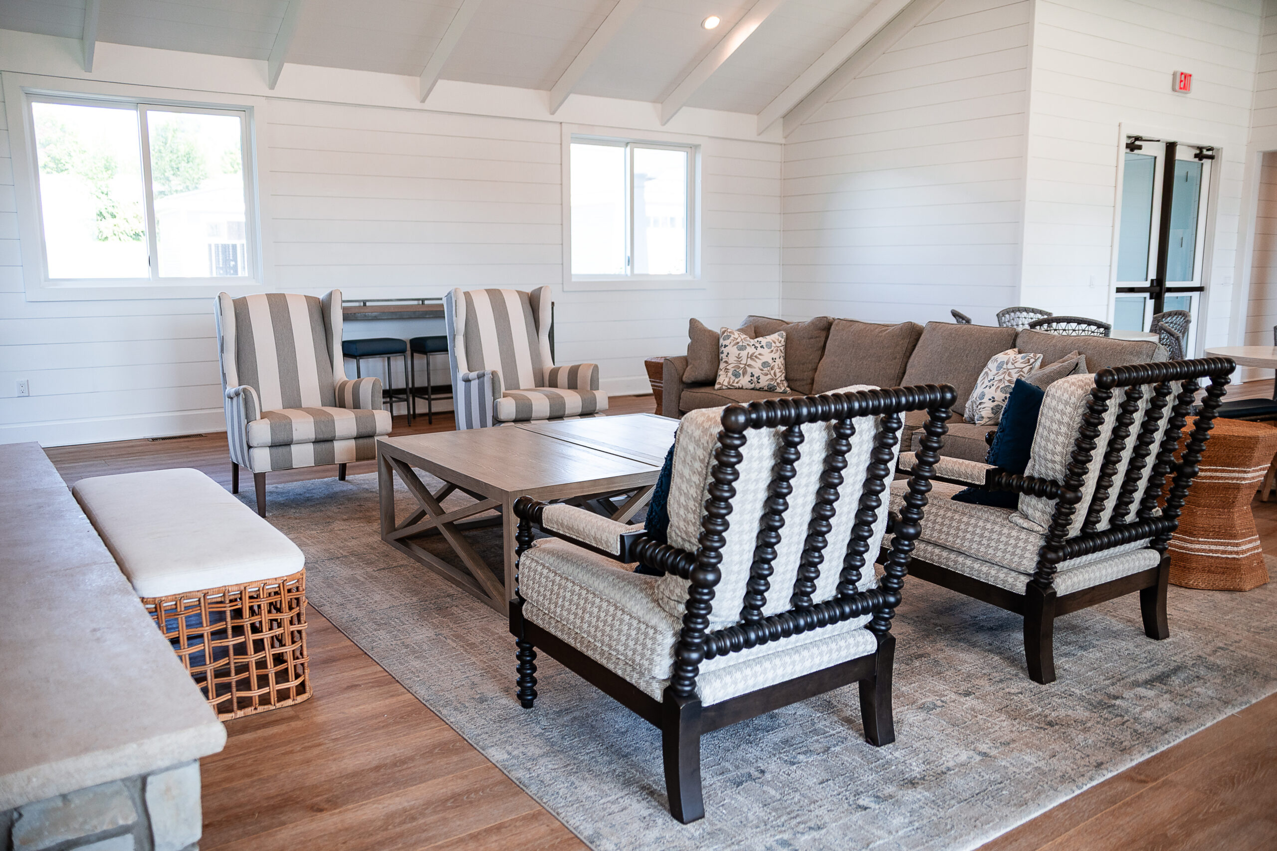 A living room in Lakeview Village features two striped armchairs, a tan sofa, two accent chairs, a wooden coffee table, and a gray rug on wood flooring.