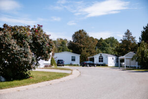 A quiet residential street in Lakeview Village with several single-story white houses, parked cars, trees, and a clear sky.