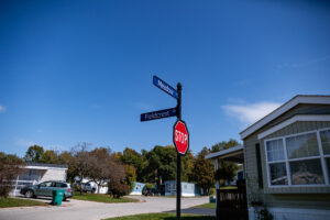 A stop sign stands at the intersection of Meadow and Fieldcrest Drive in Lakeview Village, a residential neighborhood with mobile homes under a clear blue sky.