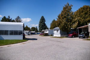 Lakeview Village is a mobile home park with several trailers, parked cars, and trees under a blue sky with scattered clouds.