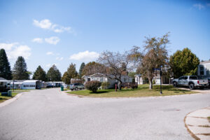 A suburban street in Lakeview Village with single-story homes, parked cars, green lawns, and trees under a clear blue sky.