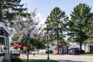 A suburban street in Lakeview Village with a "Highland St" sign, trees, parked cars, and houses visible on a sunny day.