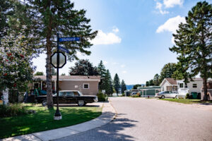 A suburban street corner in Lakeview Village with a Highland street sign, a stop sign, parked cars, and single-story houses under a sunny sky with scattered clouds.
