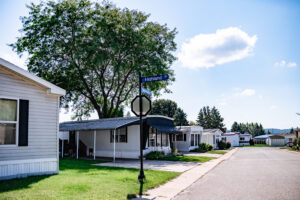 A row of mobile homes lines a quiet street in Lakeview Village on a sunny day, with a "Highland" street sign and stop sign visible in the foreground.