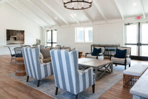 A bright, modern lounge at Lakeview Village features striped armchairs, a gray sofa, a wooden coffee table, and large windows that fill the space with natural light.