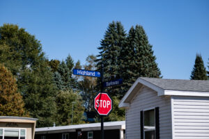 A street sign at the intersection of Highland Dr and Barkway in Lakeview Village, a residential area with trees, a stop sign, and a white house visible.